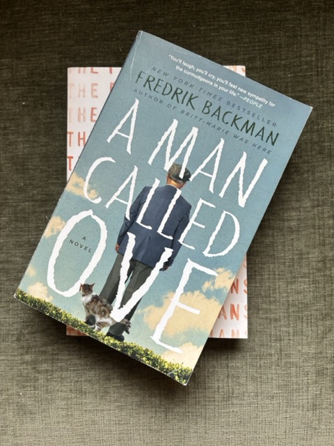 A Man Called Ove by Fredrick Backman sits atop another book on a green velvet couch cushion