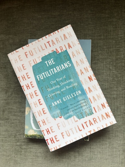 The Futilitarians by Anne Gisleson sits atop another book on a green velvet couch cushion