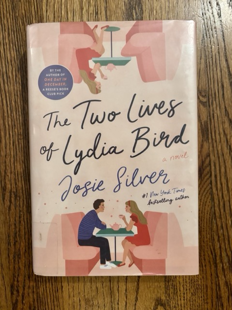 A pink, illustrated book cover, "The Two Lives of Lydia Bird," pictured on a hardwood floor